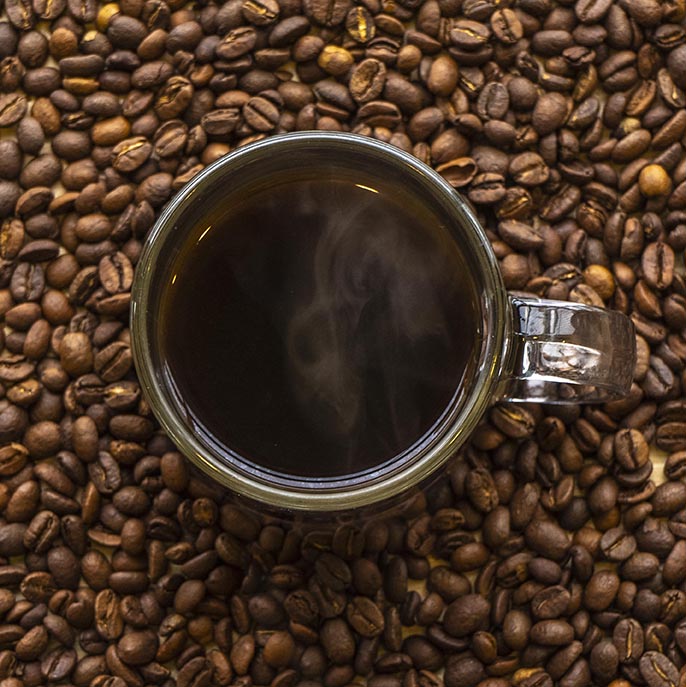Overhead of coffee in mug surrounded by coffee beans.